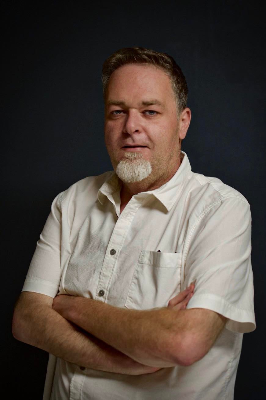 Portrait de Fabrice Deboit, fondateur de FDigital.be, bras croisés sur fond sombre.